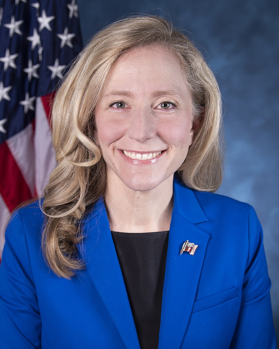 Official portrait of Abigail Spanberger in a blue jacket with a U.S. flag behind her