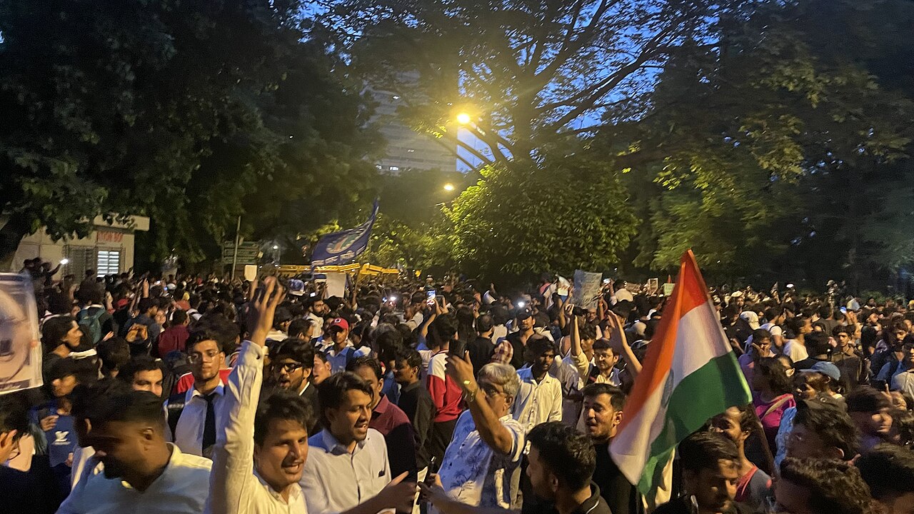 Demonstrators gather at dusk at Jantar Mantar in New Delhi, with an Indian flag in the foreground.
