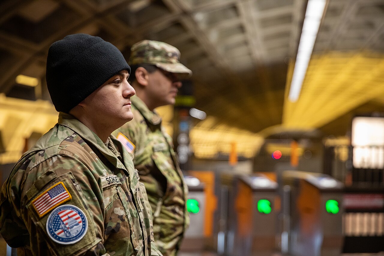 Two uniformed National Guard soldiers standing beside fare gates in a Washington, D.C. Metro station.